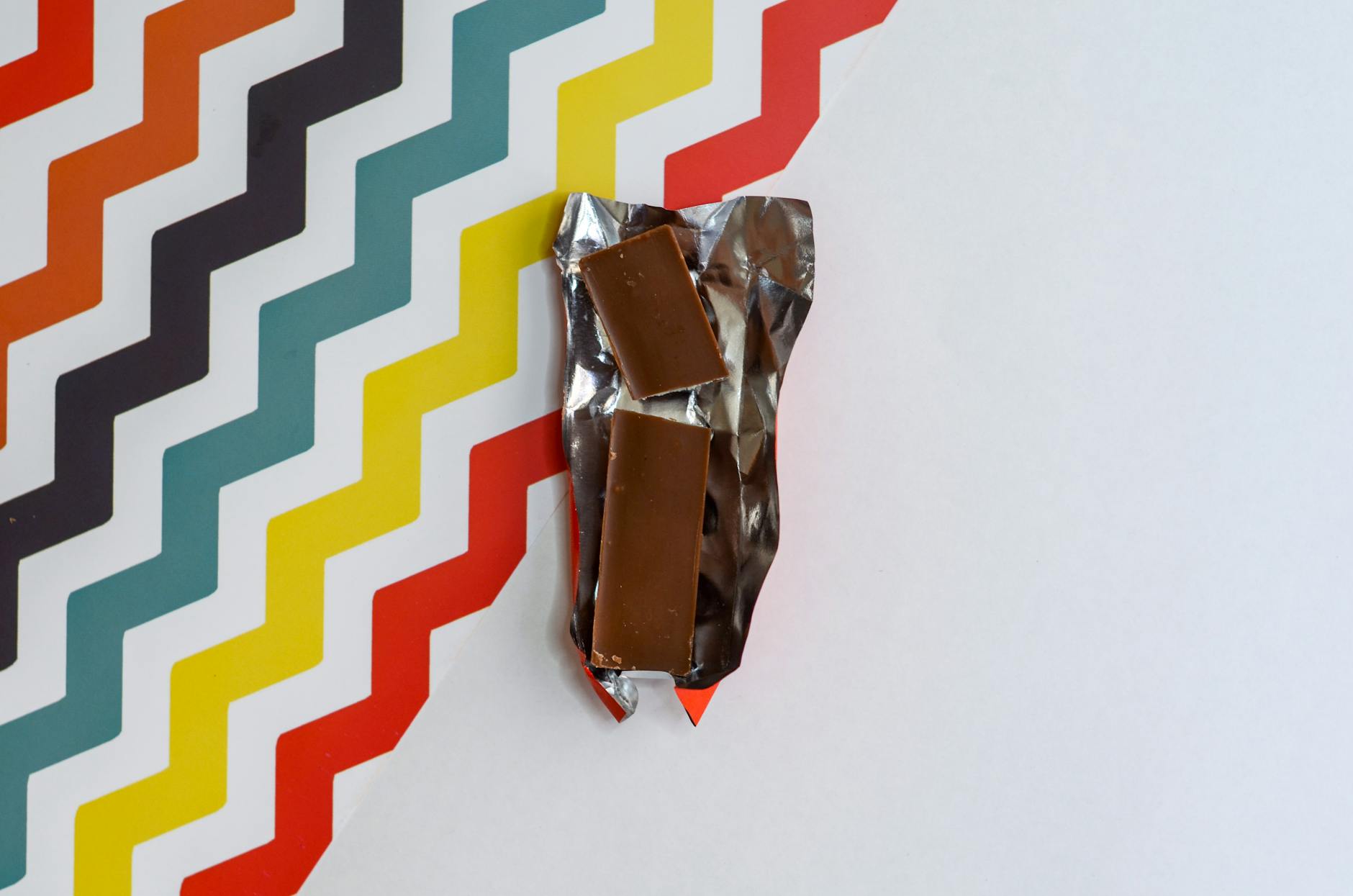 Chocolate bar unwrapped on vibrant zigzag background, showcasing bold design and indulgence.