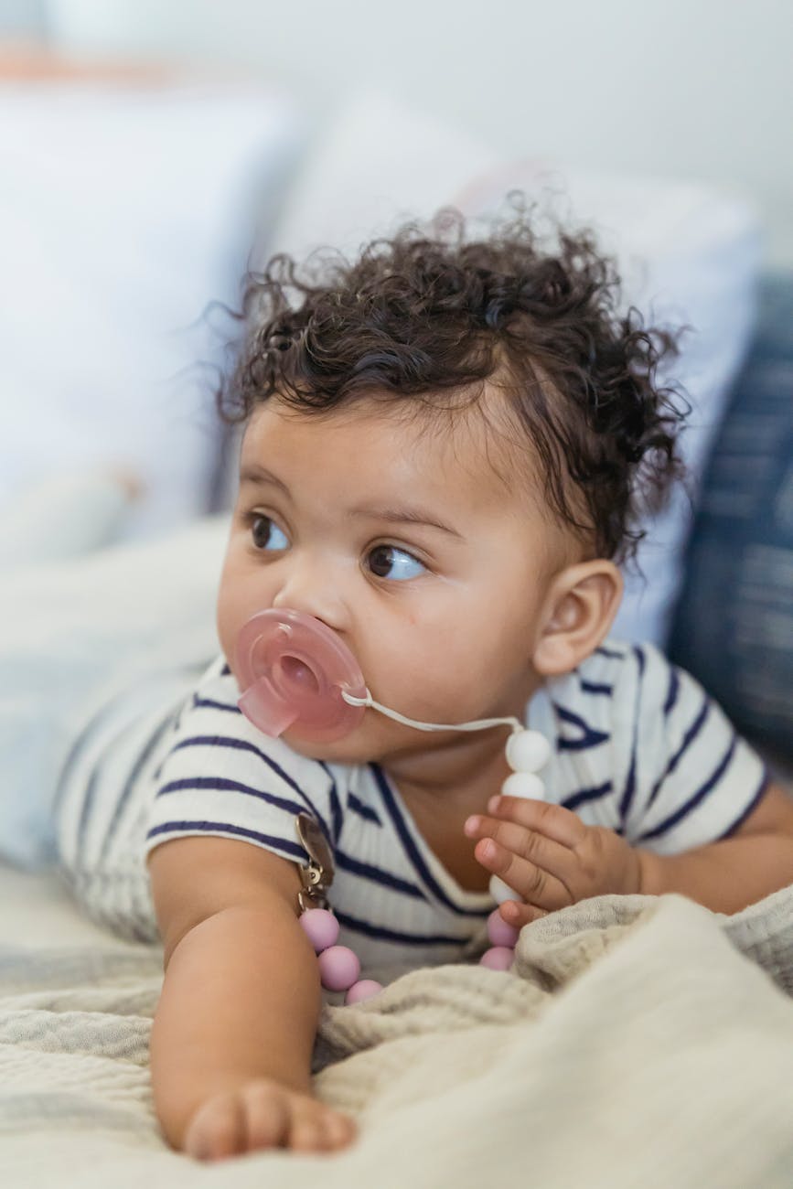 Adorable African American baby with curly hair looking away while lying on soft blanket on couch on blurred background at home