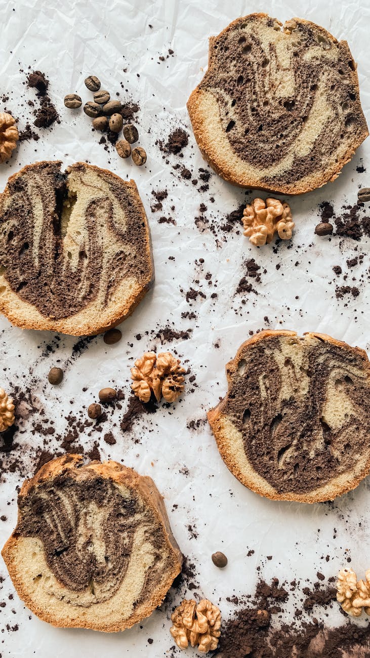 Top view of chocolate marble cake slices surrounded by coffee beans and nuts on a white background.