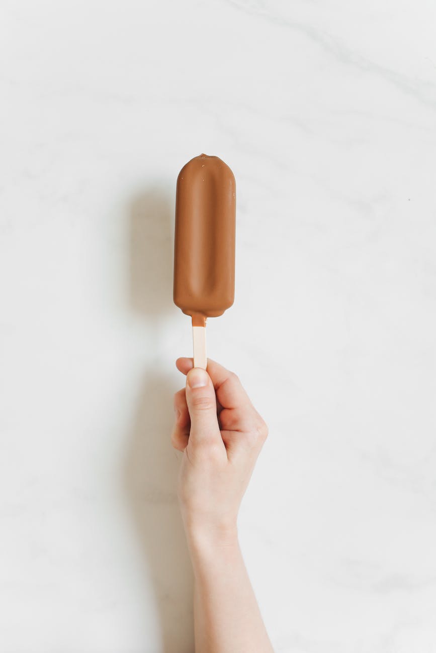 Close-up of a hand holding a chocolate-covered ice cream bar against a white background.