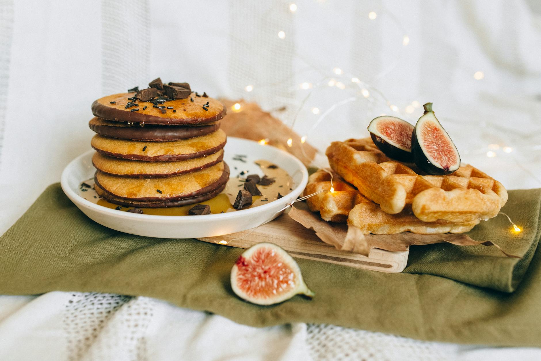 Tasty pancakes and waffles served with chocolate and fresh figs on a cozy setup.