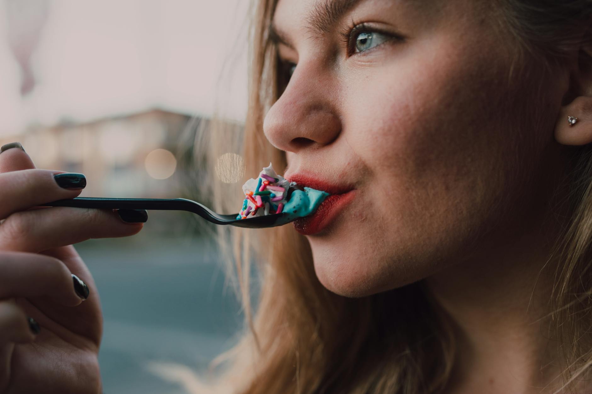 Young woman savoring a colorful dessert outdoors with vibrant sprinkles in focus.