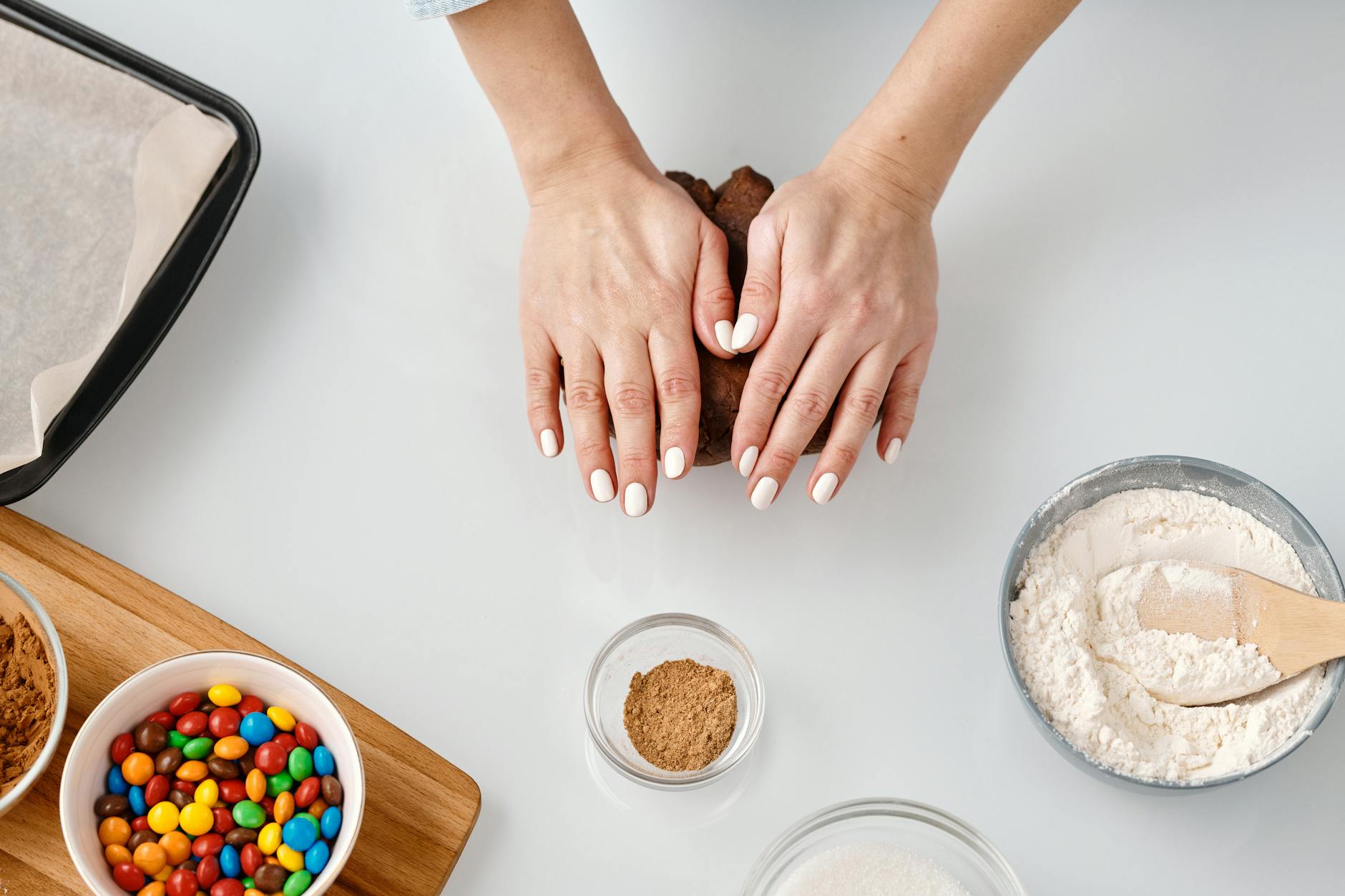 A woman kneads cookie dough with baking ingredients on a white surface. Ideal for food blogs and recipes.