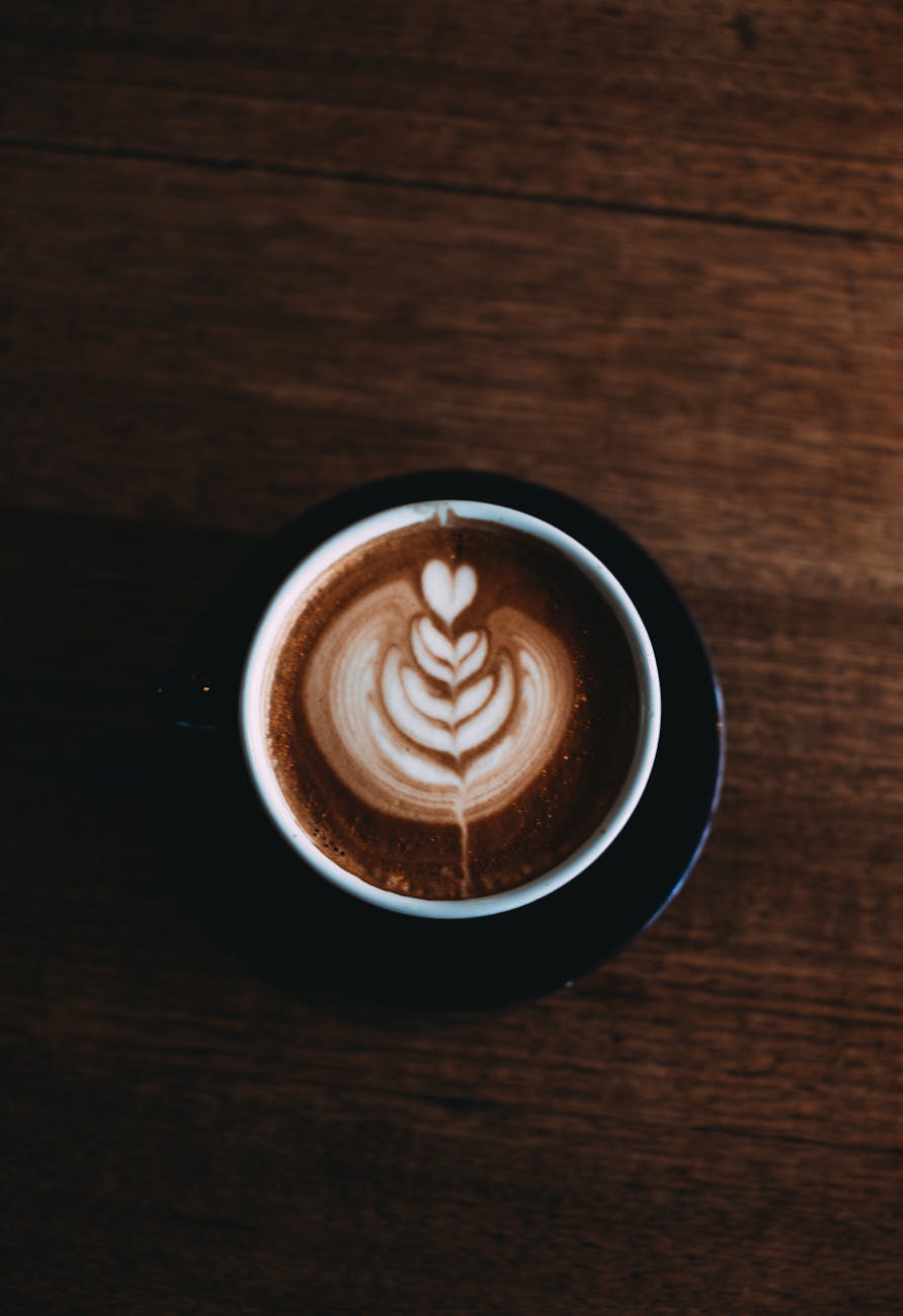 A top view of a cappuccino cup with intricate latte art sitting on a rustic wooden table.